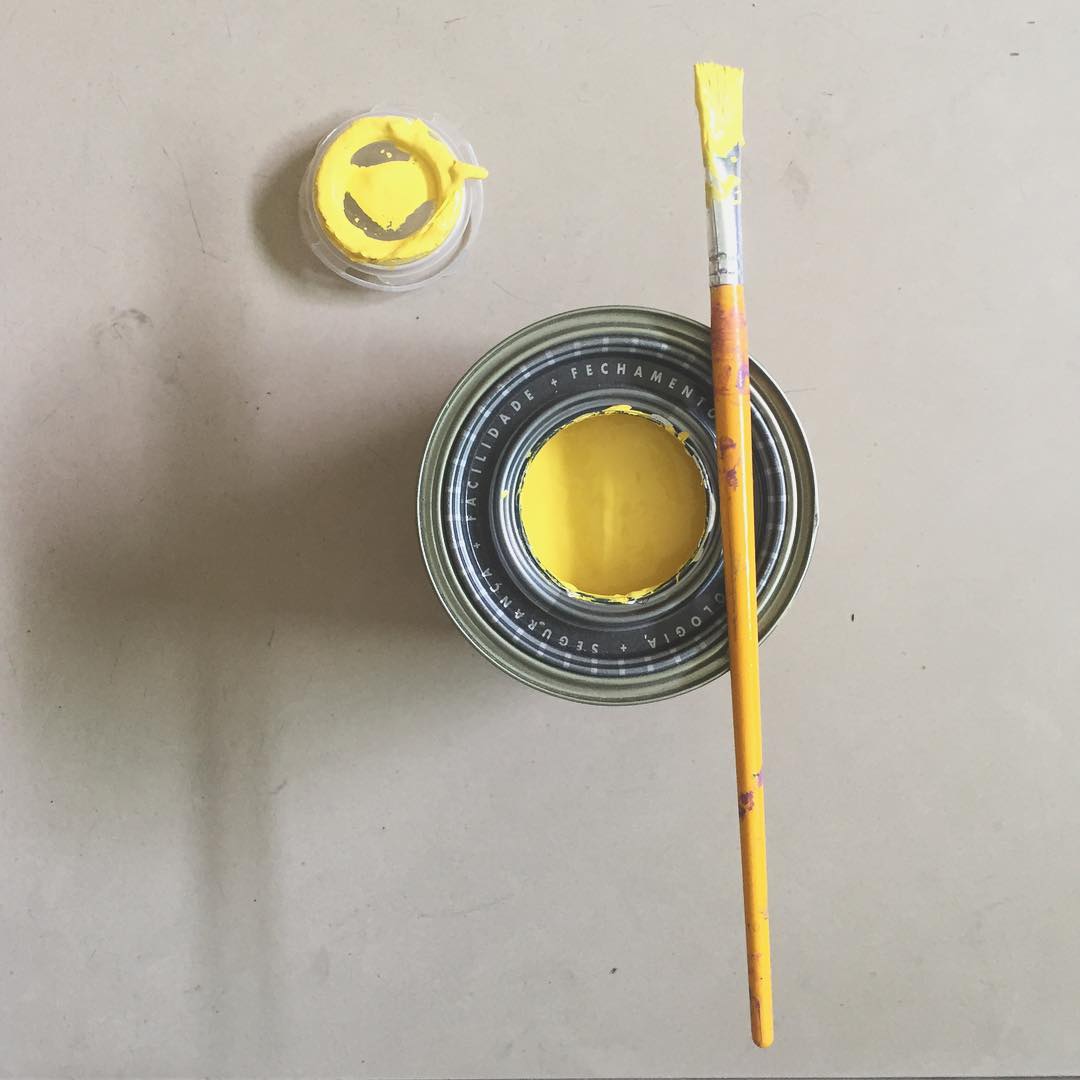 Lata de tinta amarela e pincel vistos de cima