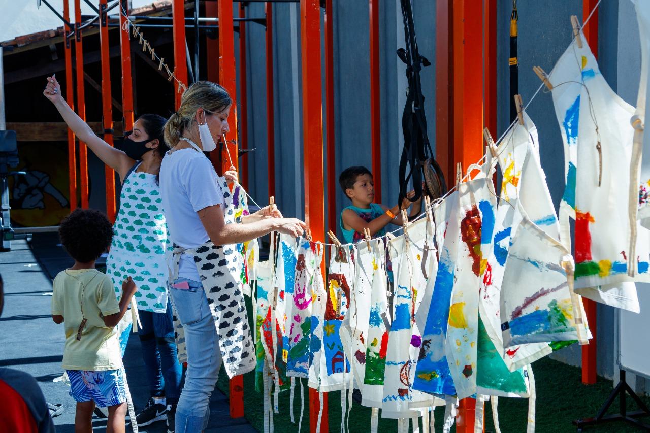 Aventais pintados pelas crianças secando no varal, com duas monitoras de avental estampado de nuvens